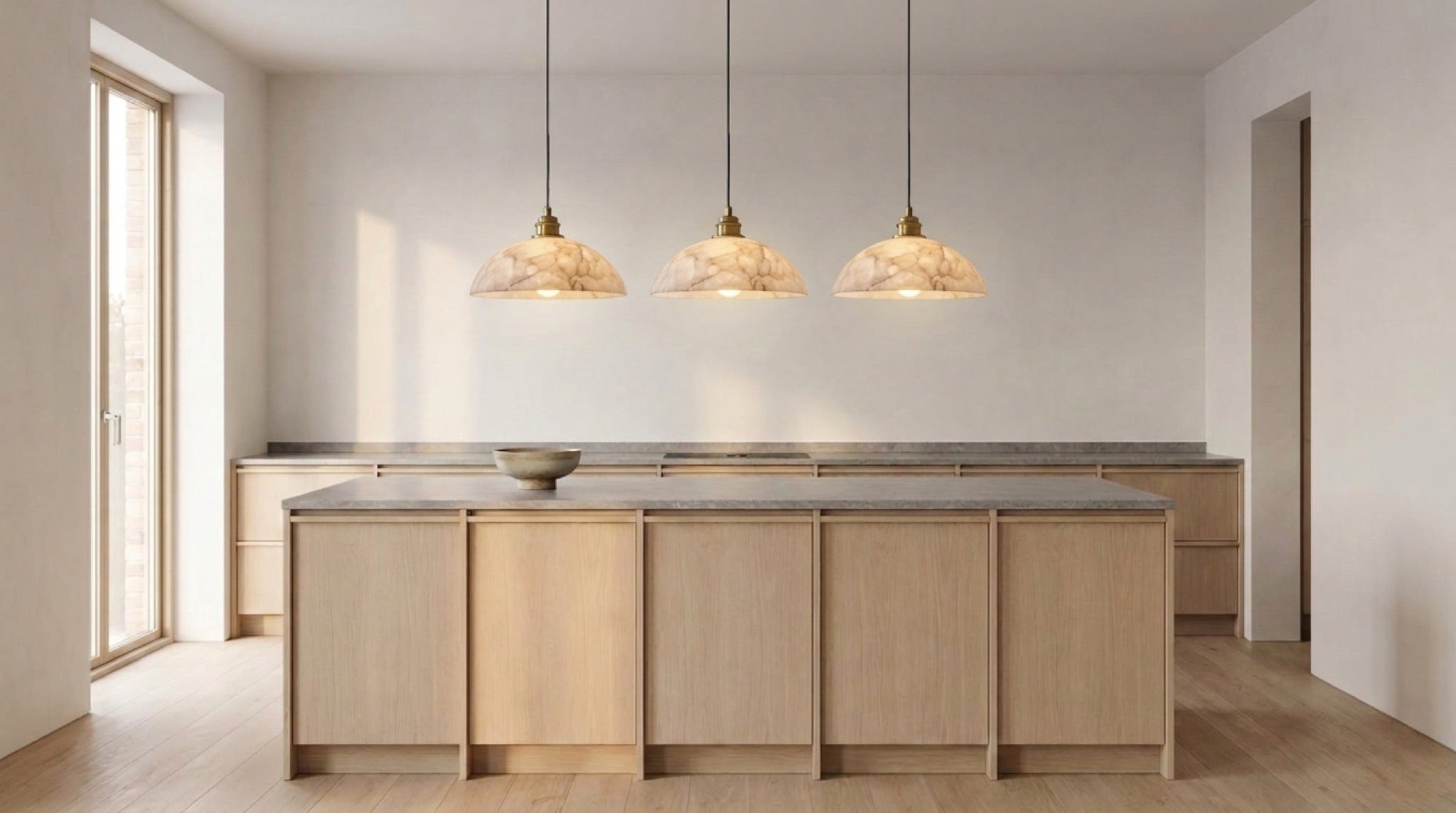 Tres lámparas colgantes con cúpulas de alabastro sobre una isla de cocina bañada por la luz de la tarde.